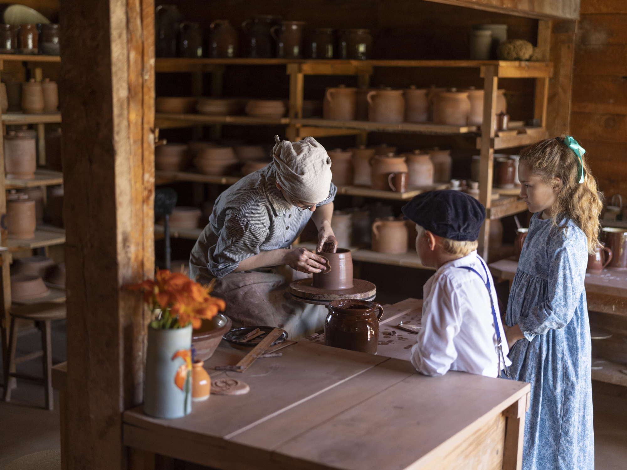Two children in costume watching a potter work.