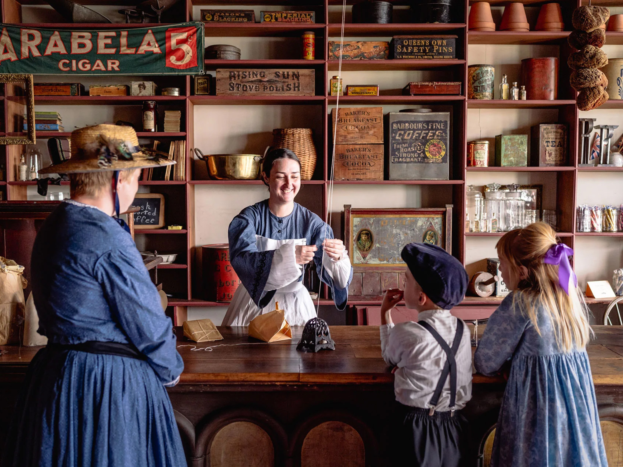 Costumed interpreter in a shop serves a woman and two children also in costume.