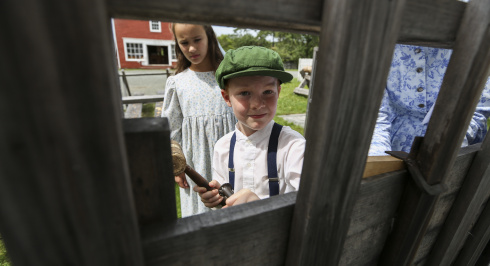 Children in costume peek though a fence.